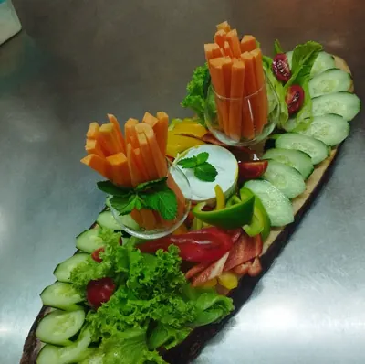 Cucumber, carrot and pepper sticks with herbs and a dip on a long wooden board