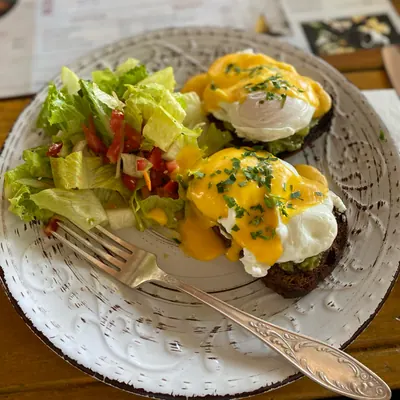 Poached eggs with hollandaise on toast and a green salad on a white plate