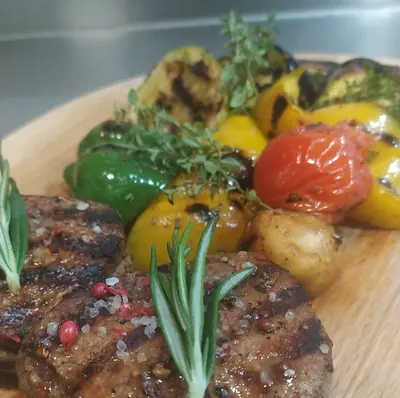A grilled steak with rosemary and roasted peppers, tomatoes and potatoes on a wooden board
